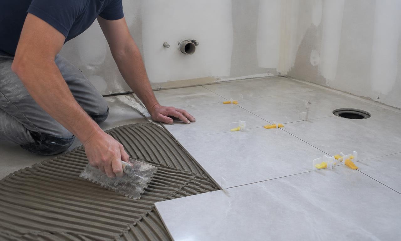 Installer setting porcelain tile with trowel and leveling spacers
